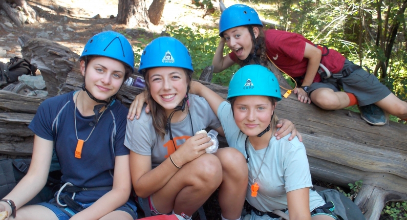 a group of outward bound students wearing blue helmets pose for a photo on a rock climbing course